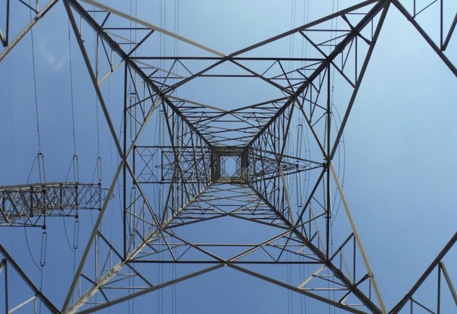 An electric transmission tower against the sky, viewed from below